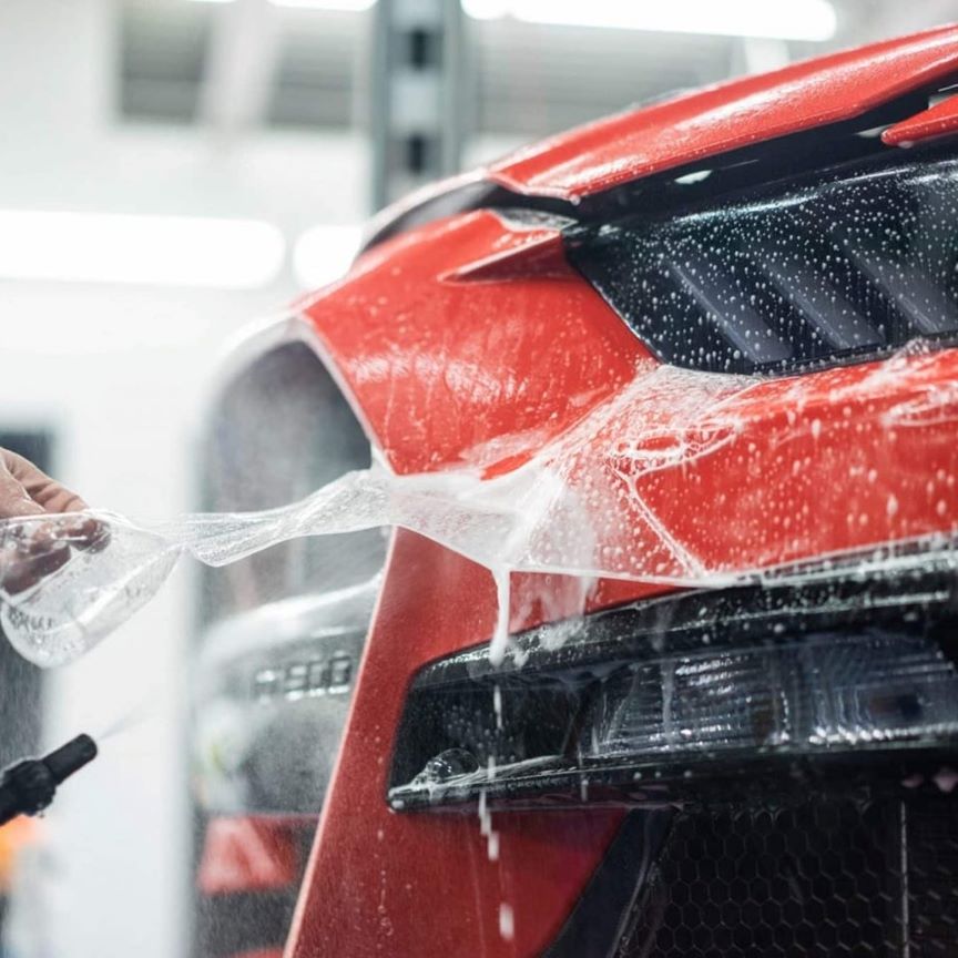 "Close-up of a hand using a high-pressure water pistol to clean a car grill